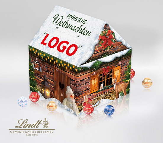 Lindt-Adventskalender in Hausform, gestaltet wie ein braunes Holzhaus mit Schnee auf dem Dach. Weihnachtlich dekoriert mit Kränzen, Lichterketten, einem Reh, Schneemann, Weihnachtsbaum und Windlicht – alles als stimmungsvolles Motiv aufgedruckt. Auf dem D