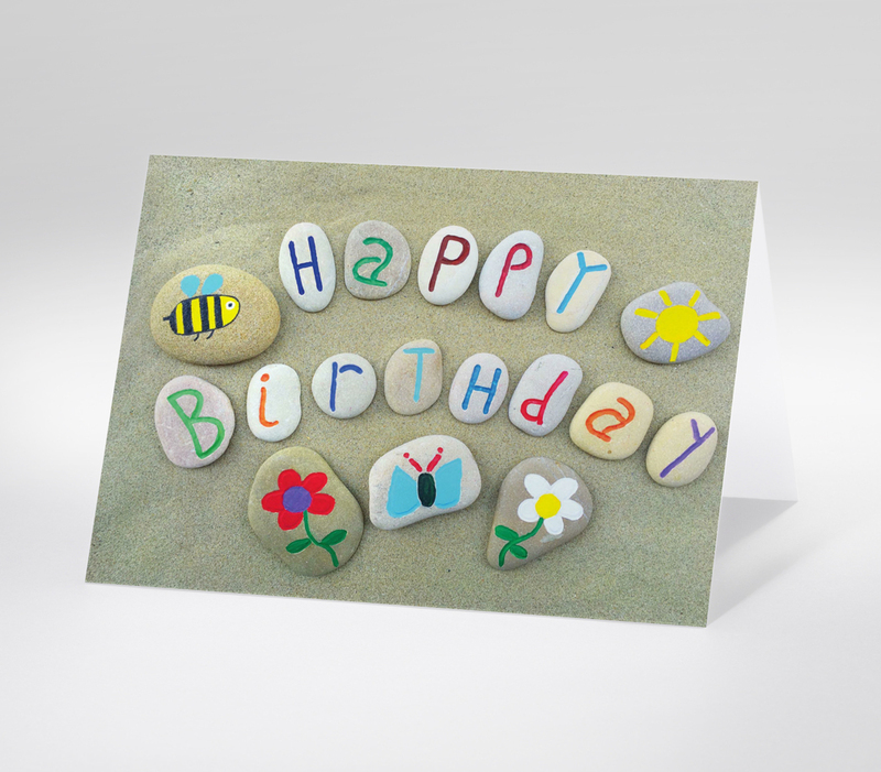 Bemalte Steine am Strand mit der Aufschrift Happy Birthday und bunten Motiven