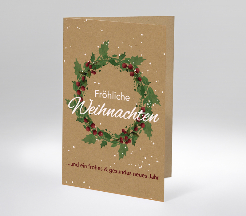 Weihnachtskarte mit grünem Kranz und Aufschrift Fröhliche Weihnachten auf braunem Karton