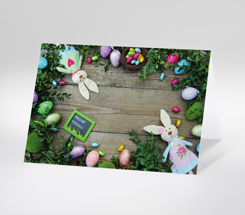 Osterdeko mit bunten Eiern, Hasenfiguren und Tafel mit Frohe Ostern auf Holzhintergrund