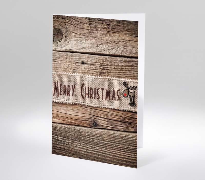 Rustikale Weihnachtskarte mit Schriftzug Merry Christmas auf Juteband vor grobem Holzhintergrund, gezeichnetes Rentier mit roter Nase