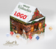Lindt-Adventskalender in Hausform, gestaltet wie ein braunes Holzhaus mit Schnee auf dem Dach. Weihnachtlich dekoriert mit Kränzen, Lichterketten, einem Reh, Schneemann, Weihnachtsbaum und Windlicht – alles als stimmungsvolles Motiv aufgedruckt. Auf dem D
