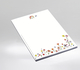 Weißes Briefpapier im A4 Format mit gezeichneter bunter Blumenwiese am unteren Rand sowie einem Ausschnitt der Blumenwiese und Schmetterling mittig am oberen Rand.
